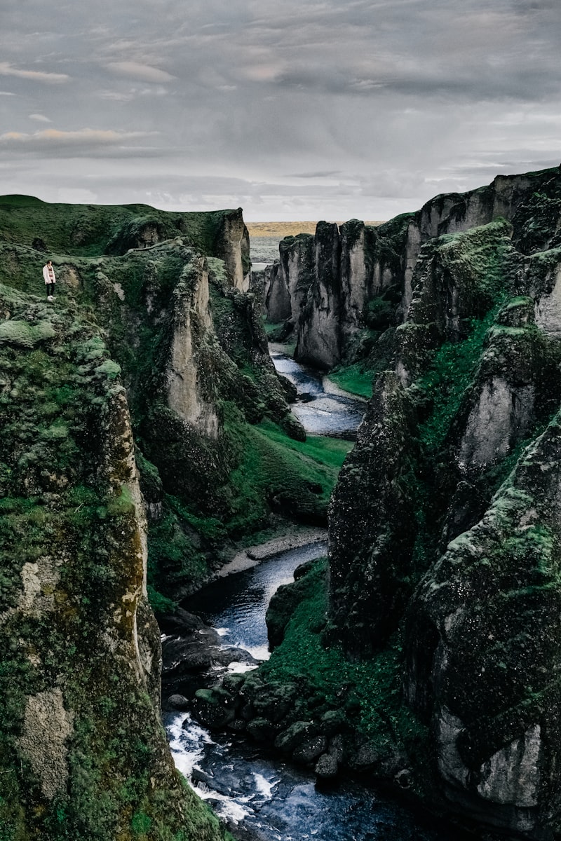 A river winding through a steep, moss-covered canyon under a cloudy sky